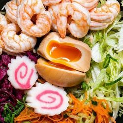 Plat asiatique avec crevettes, œuf mollet, légumes frais, carottes, salade et spirales de pâte narutomaki.