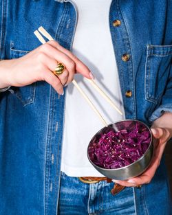 Main tenant un bol en métal avec salade de chou violet garnie de graines de sésame, utilisant des baguettes.