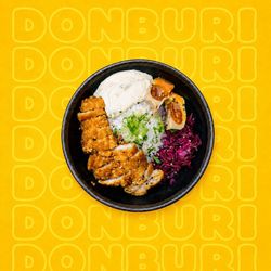 Bol de donburi avec poulet pané, riz, sauce blanche, oignons verts et légumes rouges sur fond jaune
