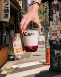 Bubble tea au lait et perles rouges tenu à la main devant un décor urbain de street food asiatique.