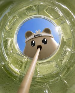 Personnage animé buvant un bubble tea vert avec paille, vu à travers le verre rempli de boisson.