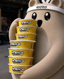 Conteneurs jaunes empilés de street food japonaise au nom Nobi Nobi devant une mascotte douce aux grands yeux noirs.