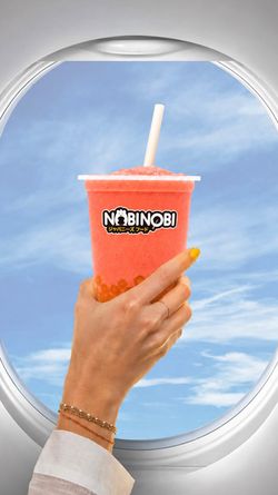 Boisson bubble tea rouge avec perles, tenue devant un hublot d'avion et ciel bleu en arrière-plan.
