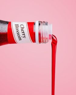 Botella de Cherry Blossom vertiendo líquido rojo sobre fondo rosa, bebida típica del restaurante Nobi Nobi Mérignac.