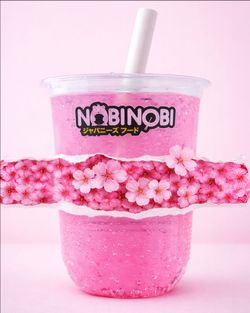 Bubble tea rose avec des perles, dans un gobelet transparent marqué du logo Nobi Nobi, fond et décor floral roses.