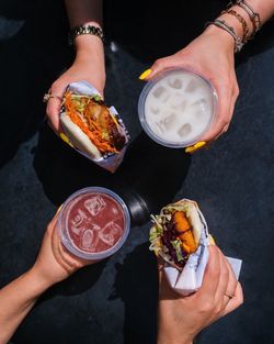 Deux bao burgers accompagnés de boissons fraîches sur fond sombre, mains tenant les aliments vues du dessus.