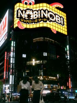 Enseigne lumineuse Nobi Nobi Tours dans une rue animée la nuit avec des piétons et des voitures visibles.