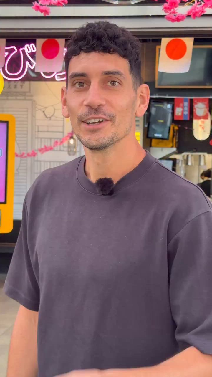 Homme en t-shirt noir devant un restaurant asiatique avec décoration japonaise visible en arrière-plan.