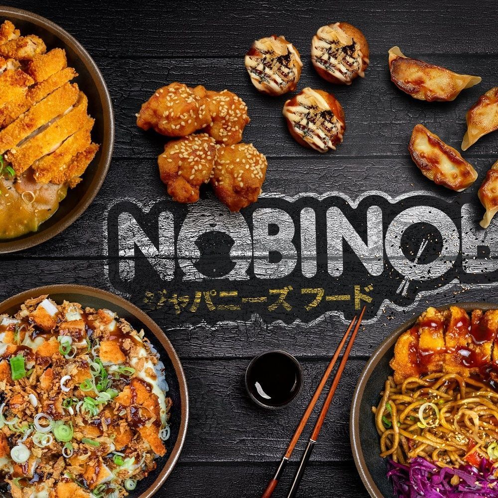Assortiment japonais avec nouilles, poulet frit, gyozas et brochettes sur table noire au restaurant Nobi Nobi Bayonne.