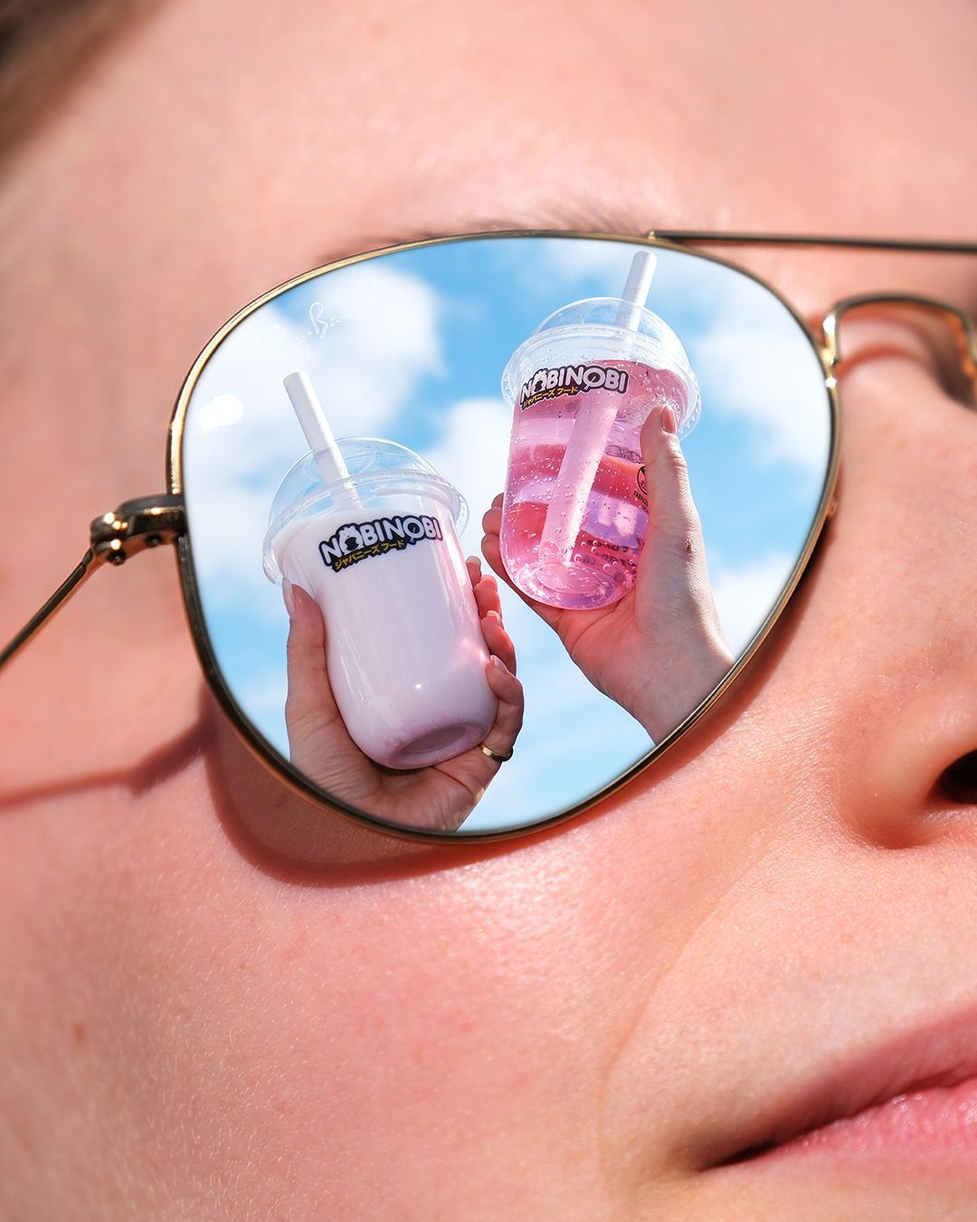 Bebidas bubble tea en vasos con logo Nobi Nobi reflejados en gafas de sol frente a un cielo azul