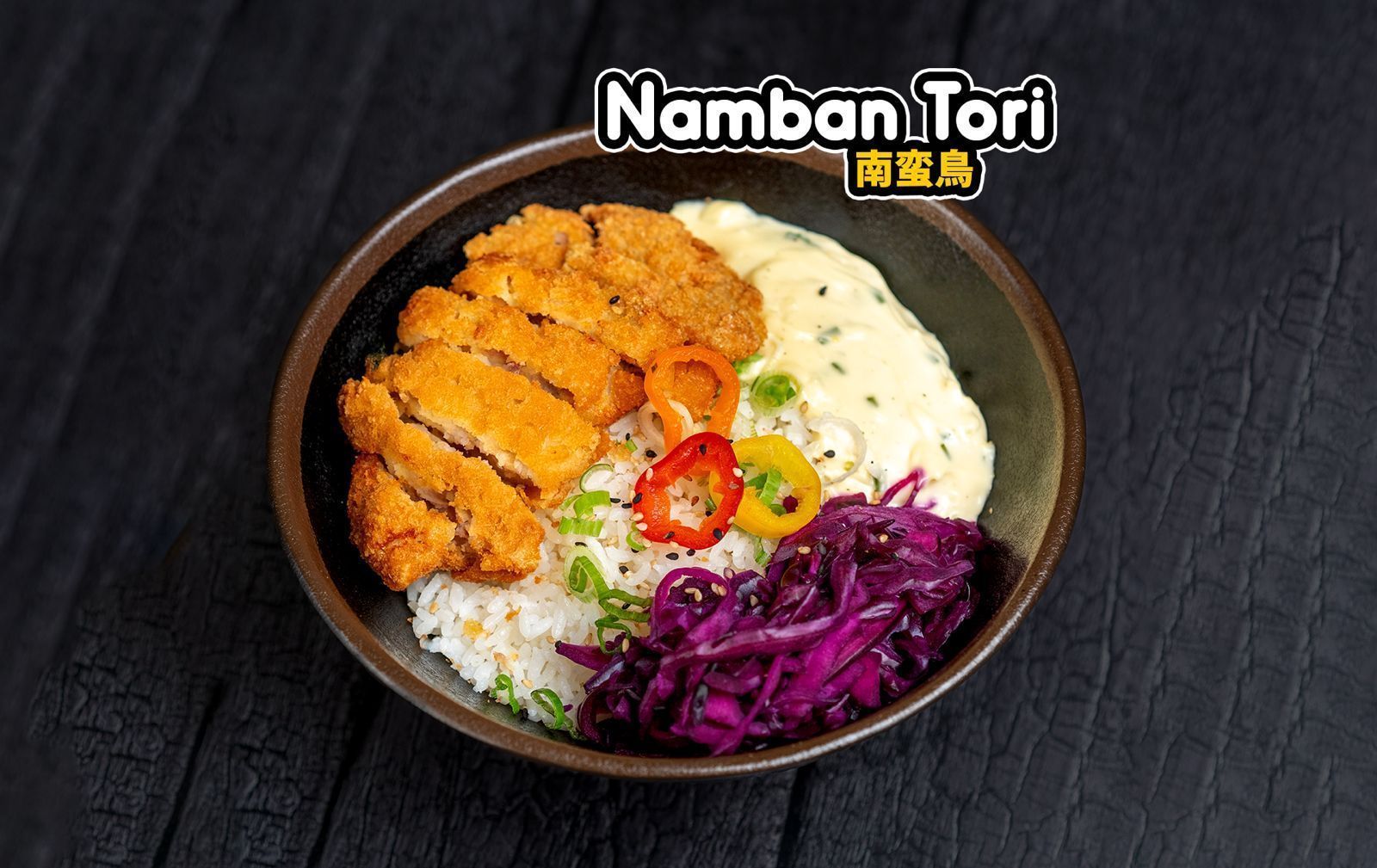 Bol asiatique avec poulet frit, chou rouge mariné, riz et sauce mayonnaise présentés sur une surface noire