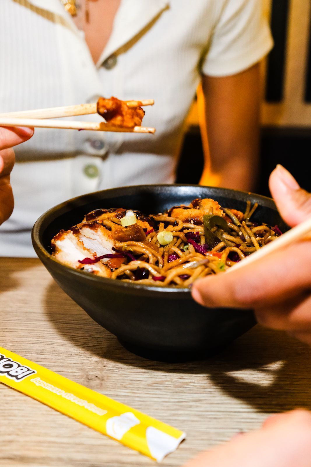 Bol de nouilles asiatiques avec morceaux de viande, servi dans un restaurant asiatique avec baguettes en main.