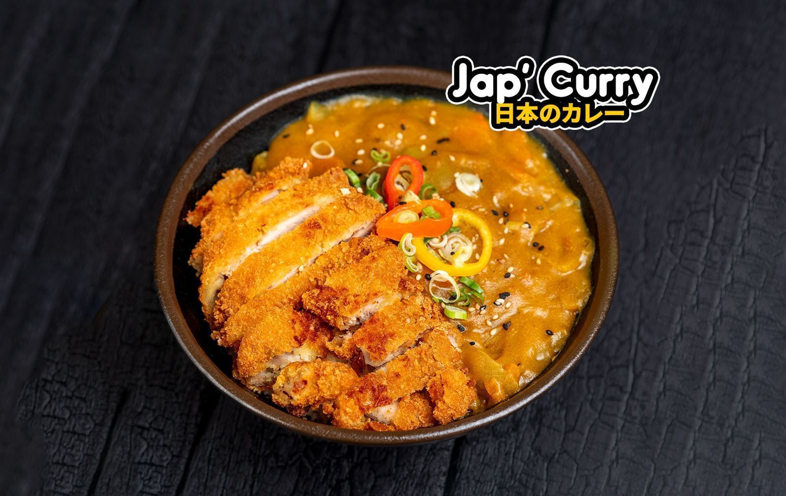 Plat de curry japonais avec poulet pané croustillant, servi dans un bol noir sur fond sombre.